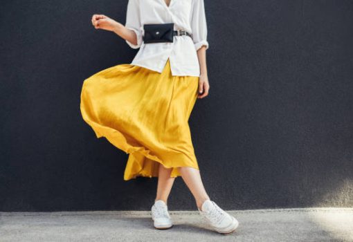 Horizontal cropped image of stylish slim woman in beautiful yellow skirt. Caucasian female fashion model standing over gray wall background outdoor with copy space.